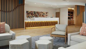 A modern reception area with a wooden reception desk, a colorful abstract wall art, and a seating area with sofas and hexagonal stools. - Springhill Suites By Marriott Ventura Oxnard (Oxnard)
