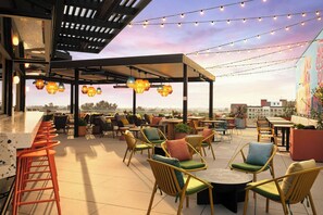 An outdoor seating area with tables and chairs, string lights, and a view of the cityscape. - Springhill Suites By Marriott Ventura Oxnard (Oxnard)