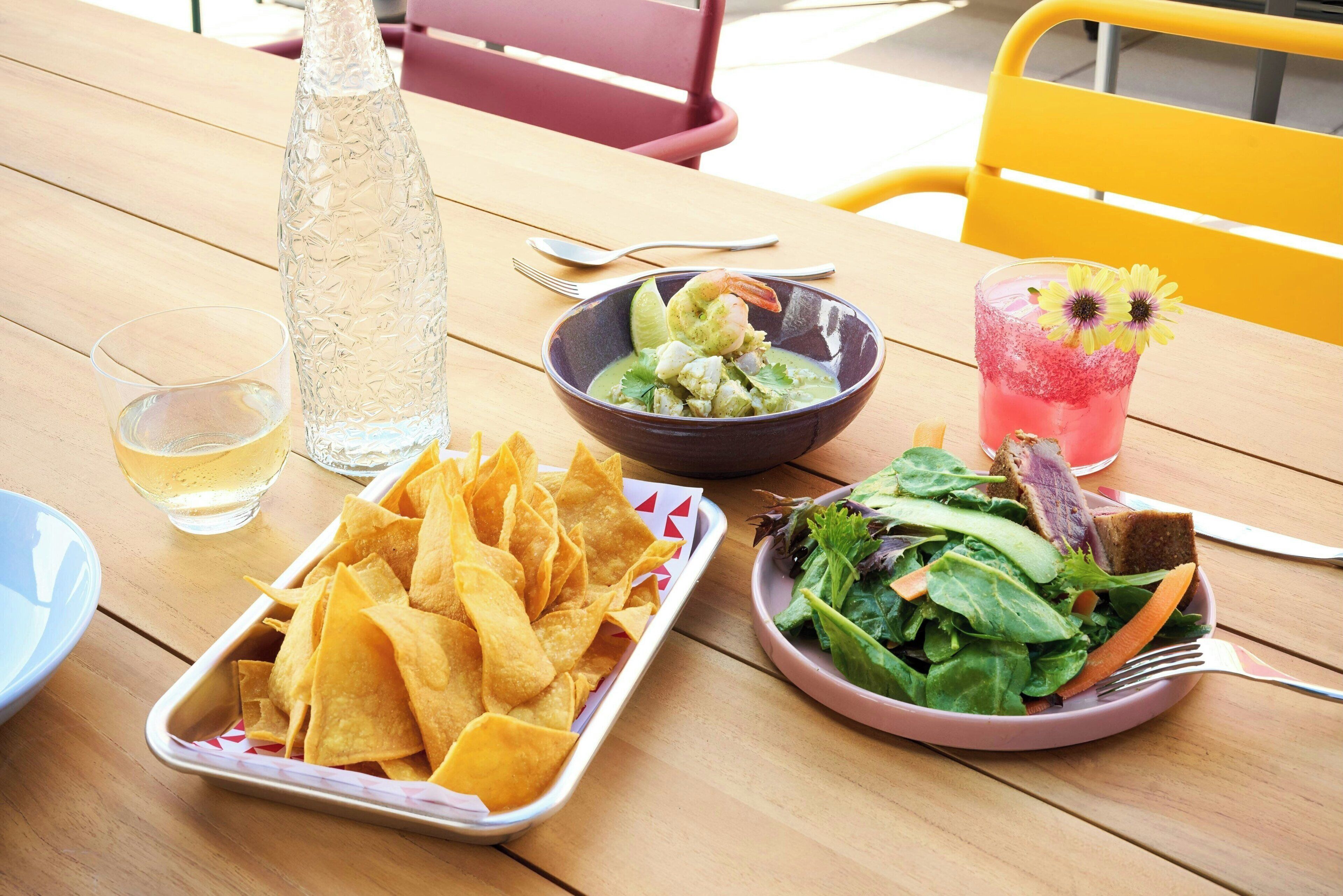 A table with a bowl of chips, a bowl of salad, a glass of drink, and a bottle of water.