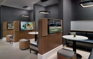 A modern lounge area with seating, tables, and a large screen displaying a sports event. - Courtyard By Marriott Birmingham Grandview (Birmingham)
