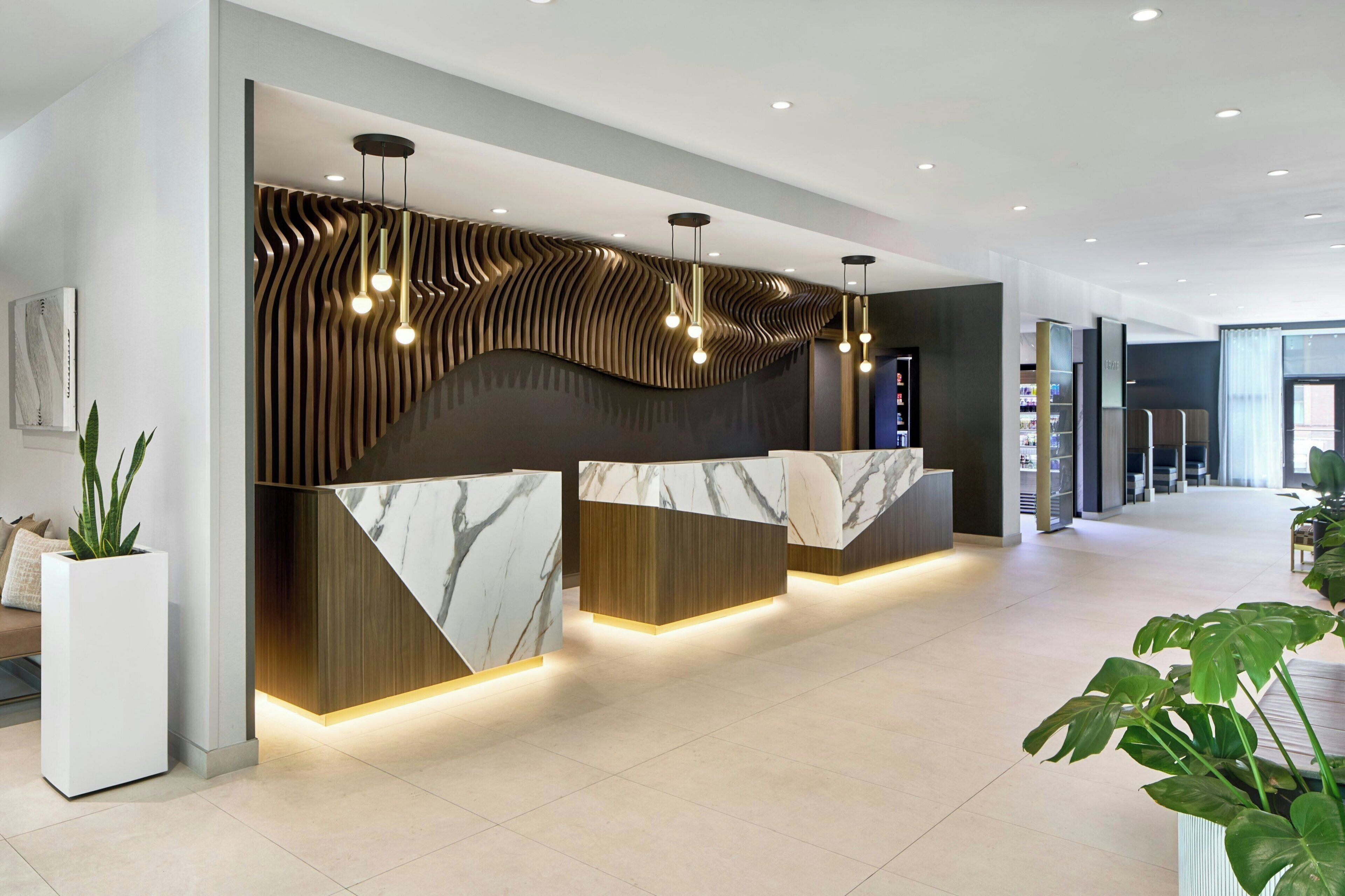 Un mostrador de recepción moderno con encimera de mármol y paneles de madera, complementado con iluminaci ón colgante.