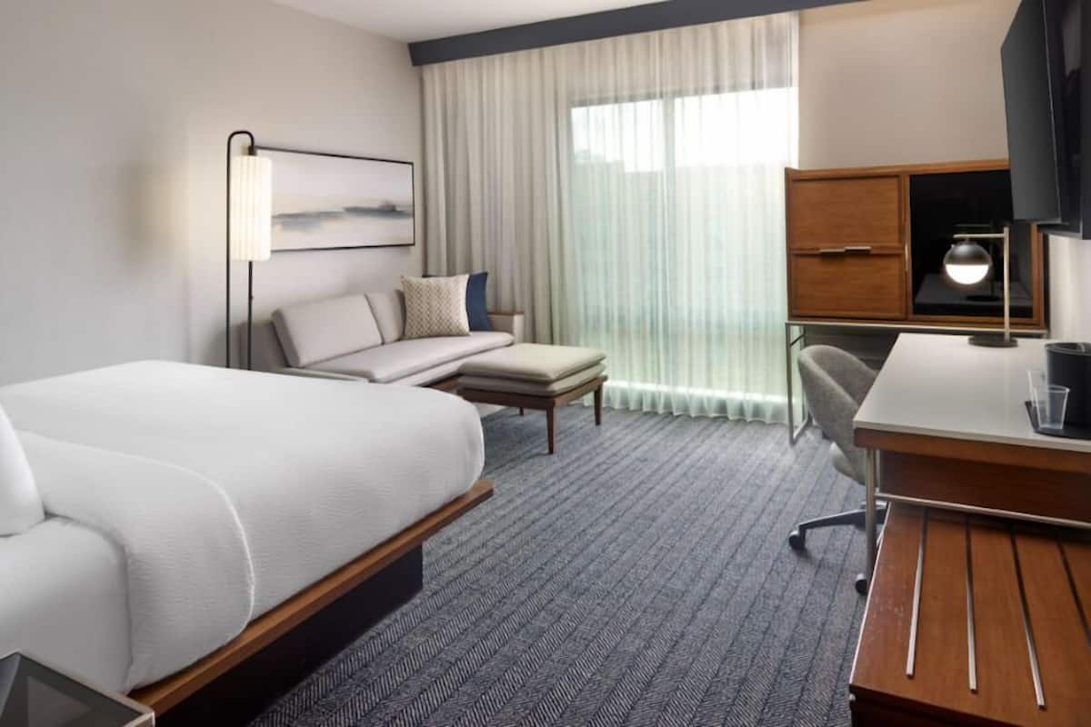 A hotel room with a bed, a desk, a chair, a television, and a window with curtains.