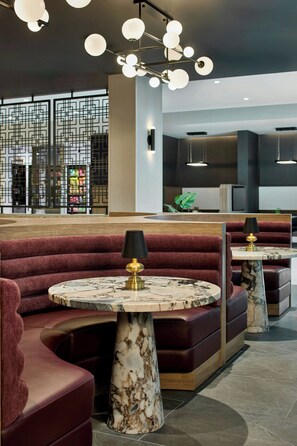 A modern interior with seating areas, marble-topped tables, and a decorative ceiling light fixture.