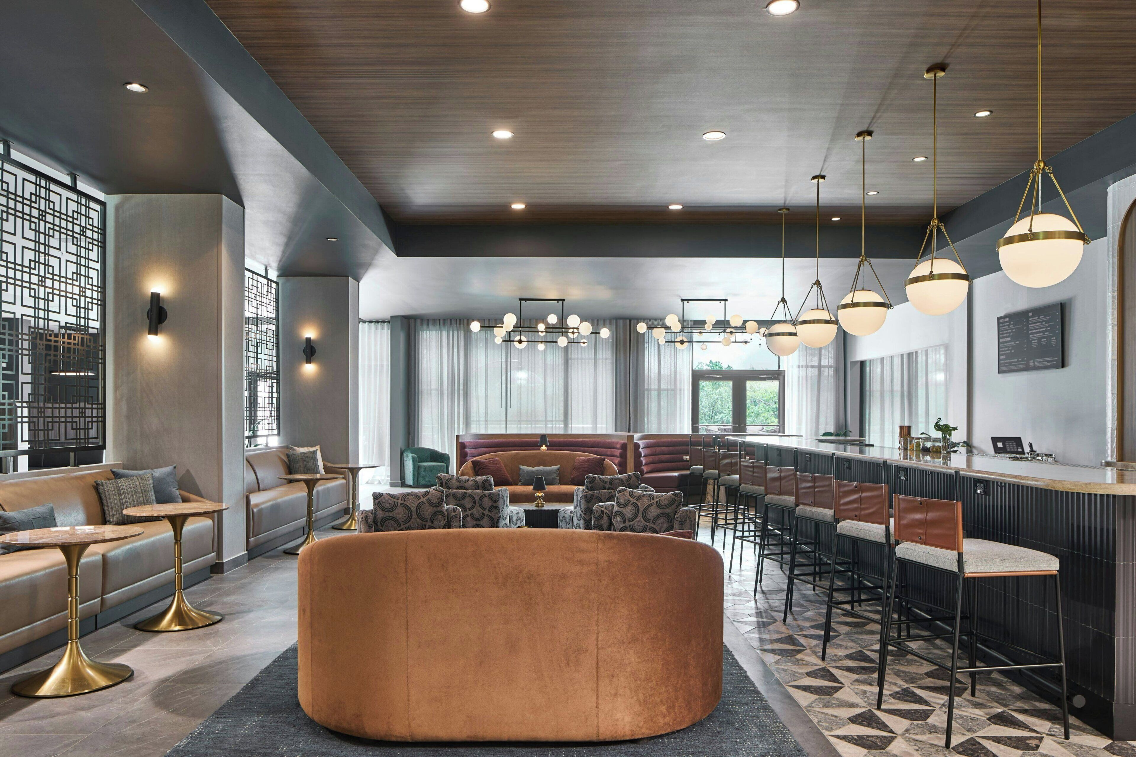 A modern hotel lobby with a bar area, seating arrangements, and a large round ottoman.