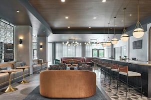 Un moderno hall de hotel con zona de bar, asientos y un otomano grande y redondo.