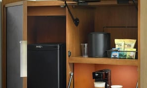 A compact kitchen with a black refrigerator, a coffee maker, and a shelf with snacks.