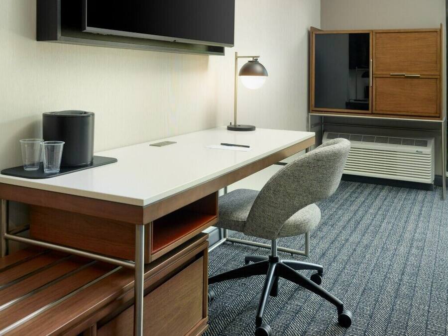 A modern office desk with a chair, a television mounted on the wall, and a cabinet with a sliding door.