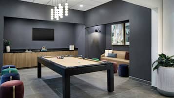 A modern indoor space with a pool table, a sofa, a coffee table, and a dining area.