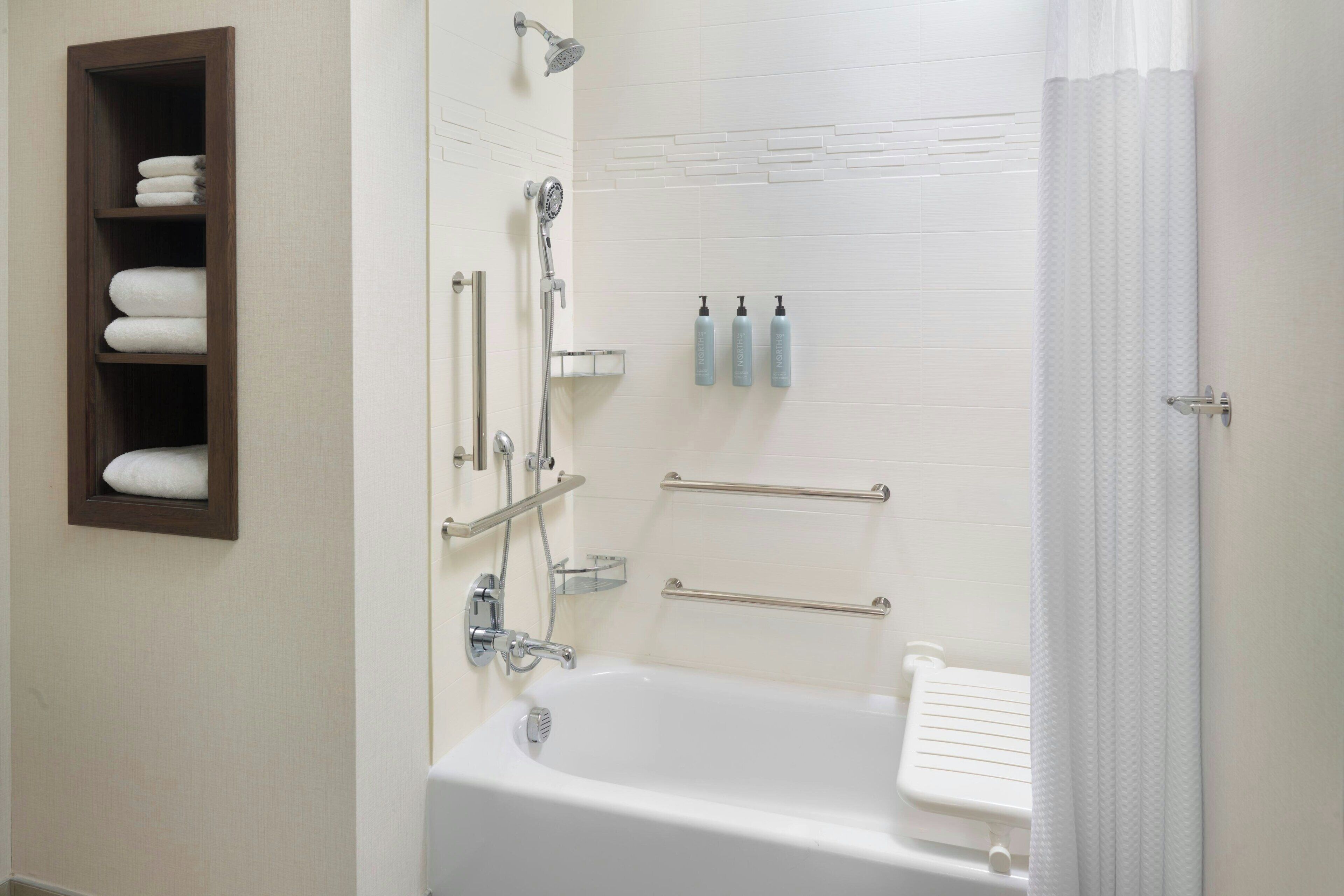A bathroom with a bathtub, shower, towel rack, and toiletries.