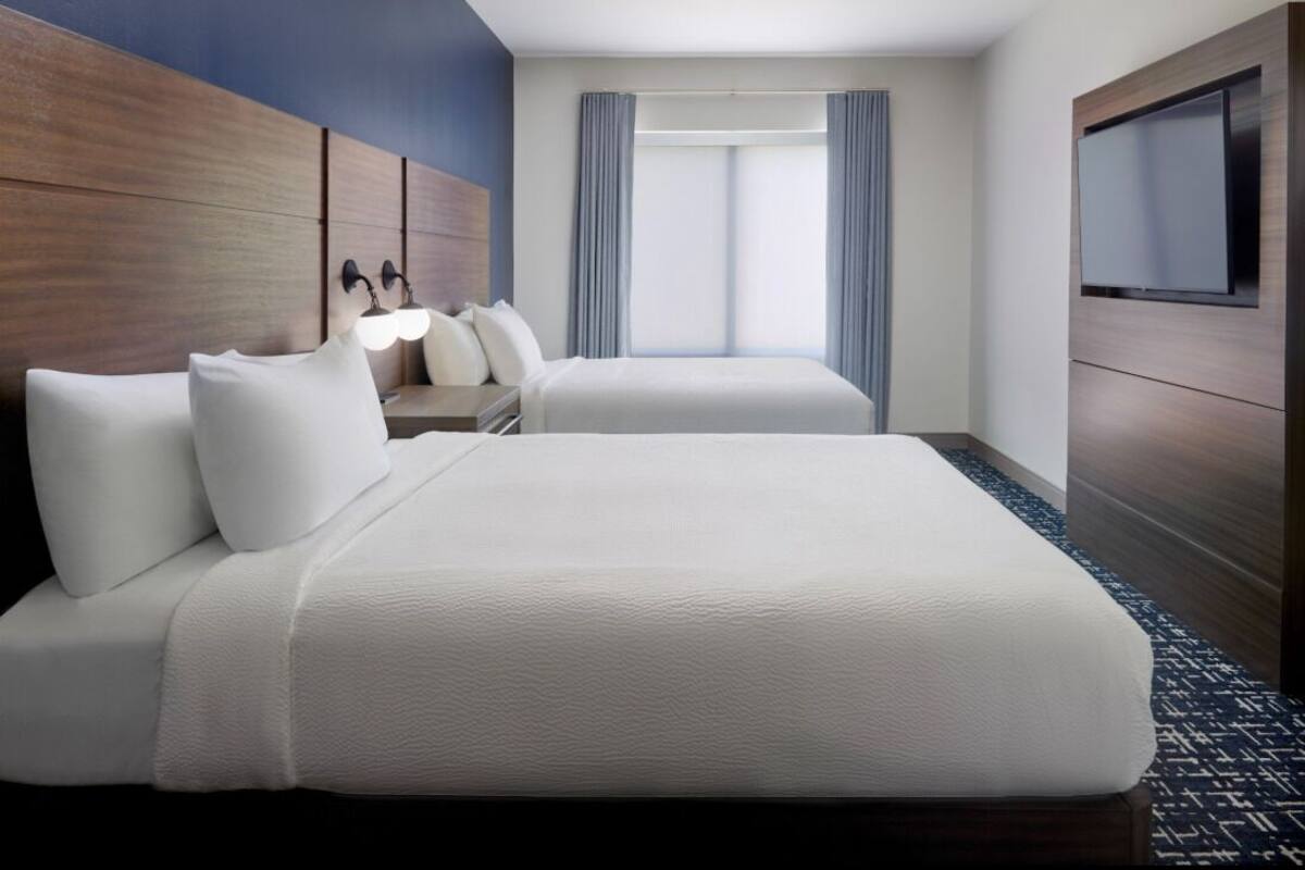 A hotel room with a bed, a TV, a desk with a chair, and a window with curtains.