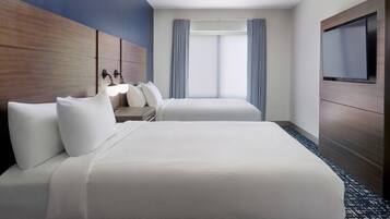 A hotel room with a bed, a TV, a desk with a chair, and a window with curtains.