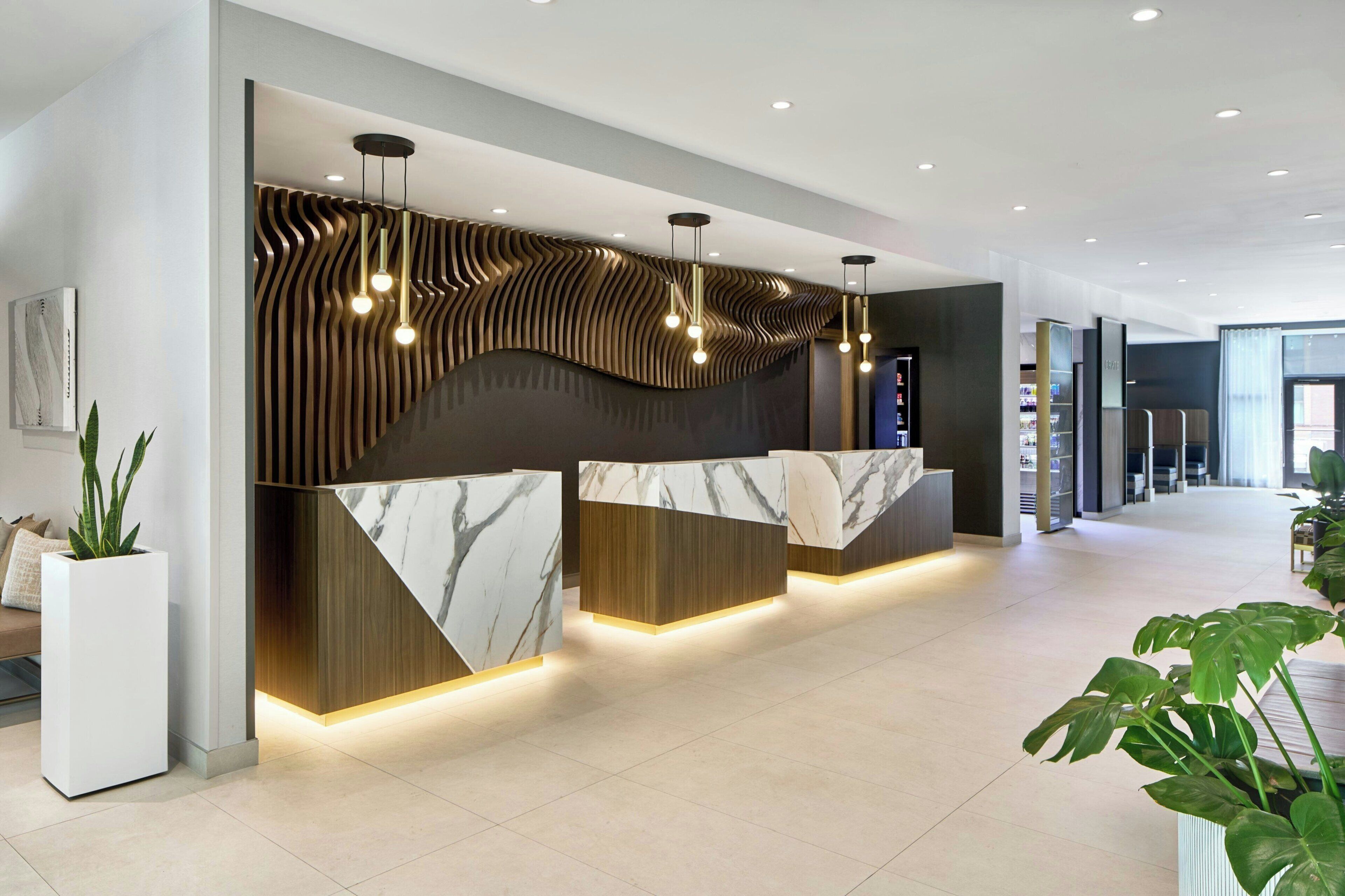 A modern reception desk with marble tops and wooden accents, flanked by vertical light fixtures.