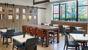 A restaurant with a long communal table, individual booths, and a large window with a view of the outside. - Residence Inn By Marriott Birmingham Grandview (Birmingham)