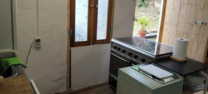 Una cocina con estufa, una ventana con vidrio esmerilado y una planta en maceta afuera.