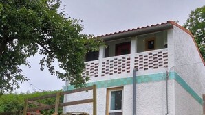 Un edificio de dos pisos con balcón, pared de piedra y cerca de madera.