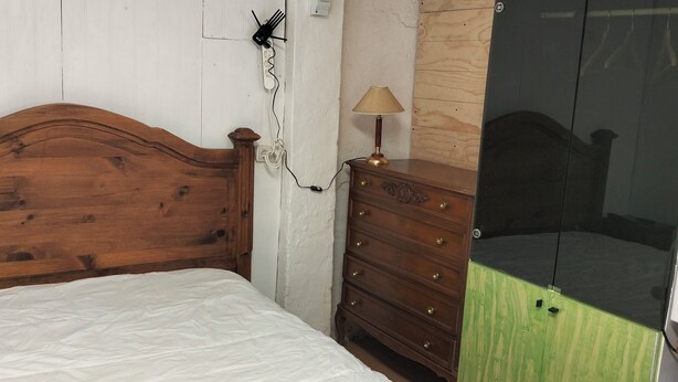 Une chambre à coucher avec une tête de lit en bois, un lit recouvert d’un drap blanc, une commode en bois et un miroir.