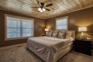 A bedroom with a bed, two bedside lamps, a ceiling fan, and large windows with blinds. - Peaceful Cabin in the Smokies - Hot Tub/Pool Table/Pinball (Sevier County)