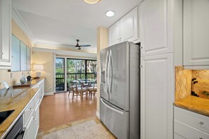 A kitchen with a large refrigerator, wooden cabinets, a dining area with chairs, and a view of the outdoors. - Beachfront Ocean View Oasis w/Saltwater Pool (Kapaʻa)