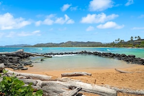 A beach with clear turquoise water, rocky shoreline, and distant mountains. - Beachfront Ocean View Oasis w/Saltwater Pool (Kapaʻa)