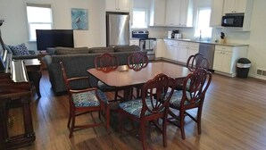 Een ruime woonkamer met een grote bank, een eettafel met stoelen en een keuken met witte kasten en apparatuur.