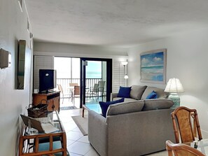 Un salon avec un canapé, un téléviseur, une lampe et une vue sur l’océan par les portes du balcon.