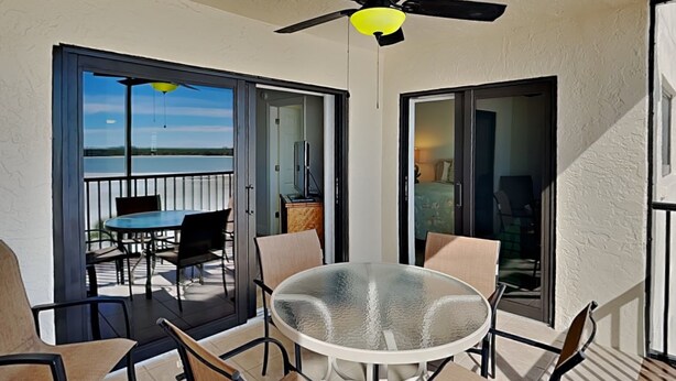 Een balkon met een glazen tafel en stoelen, een plafondventilator en uitzicht op de oceaan.