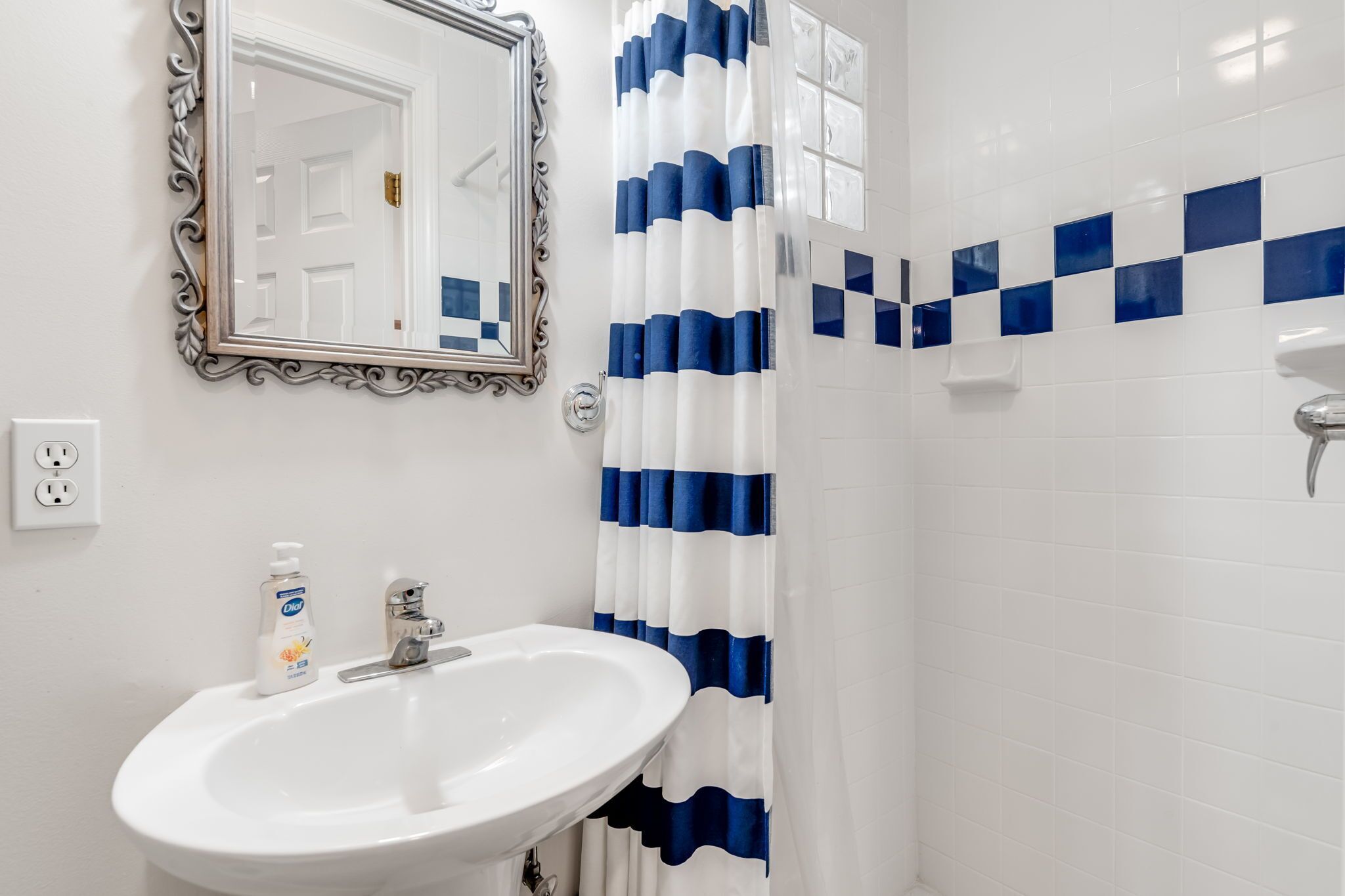 Une salle de bain avec un lavabo blanc, un miroir doté d’un cadre orné et un rideau de douche à rayures bleues et blanches.
