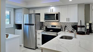 A modern kitchen with white cabinets, stainless steel appliances, a microwave, a toaster, and a sink. - Carlos Pointe 121 (Fort Myers Beach)