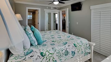 Ein Schlafzimmer mit einem Bett, einem Deckenventilator, einem Fernseher und einer Tür zu einem anderen Raum.