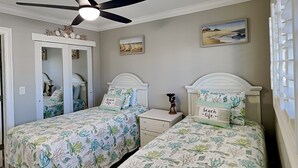 Une chambre avec deux lits, un ventilateur de plafond et une porte donnant sur une autre pièce.