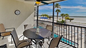 A balcony with a table and chairs, a ceiling fan, and a view of the beach and palm trees. - Carlos Pointe 121 (Fort Myers Beach)