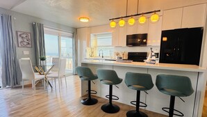 Een moderne keuken met een centraal eiland, een bar met krukken, een eethoek met een witte tafel en stoelen, en een groot raam dat voor natuurlijk licht zorgt.