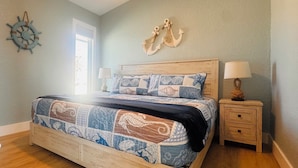 Une chambre à coucher avec un lit en bois, une literie sur le thème de la marine, une table de chevet avec une lampe et une décoration en forme d’ancre fixée au mur.
