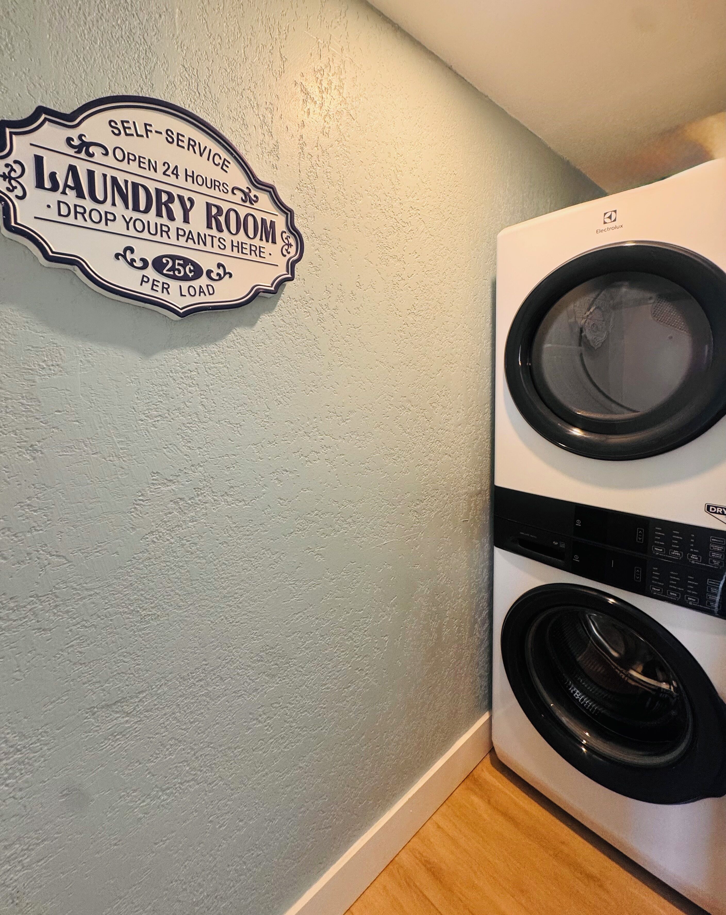 A laundry room with a sign indicating self-service, 24-hour availability, and a 25¢ per load fee.