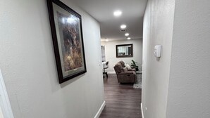 A hallway with a framed picture on the left, a ceiling light, and a couch in the background. -  The Happy Place, a Charming & Cozy 3-bedroom home in the heart of Sneads, FL. (Sneads)