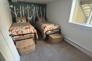 A small room with two beds, each with a woven basket at the foot, a wall mural of trees and deer, and a window with a view of a wooden structure outside. - Cozy 3-Bedroom Mountain Style Home (Reading)