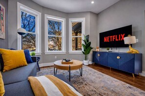 A modern living room with a large TV, a sofa, a coffee table, and a blue cabinet. - Full Home Group Getaway Sleeps 8 (Detroit)