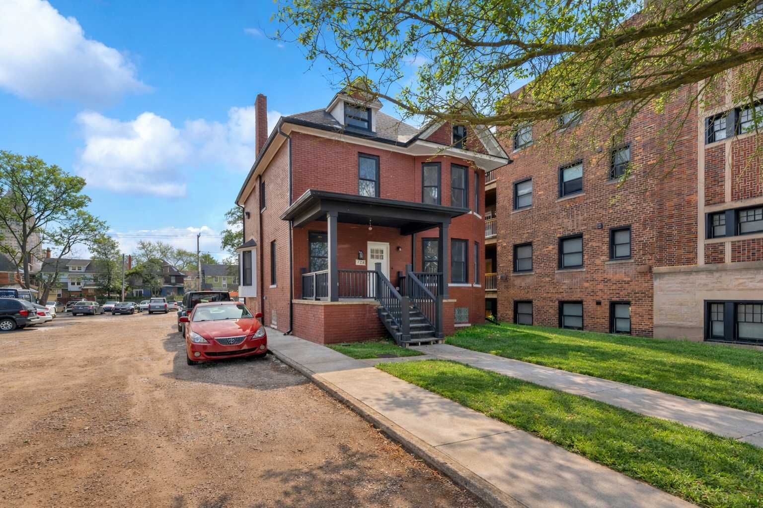 A multi-story brick building with a covered front porch and a red car parked in front.