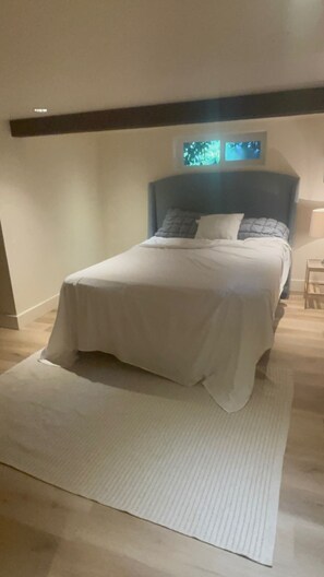Ein ordentlich bezogenes Bett mit weißer Decke und Kissen, ein kleiner Nachttisch und ein an der Wand befestigtes Fernsehgerät.