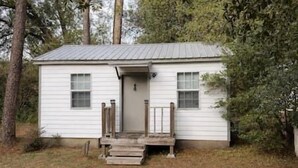 A small, single-story cabin with a front porch and a door, surrounded by trees. - Rawson Circle Cottage (Albany)