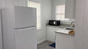 A small kitchen with white cabinets, a white refrigerator, a microwave, and a sink. - Rawson Circle Cottage (Albany)