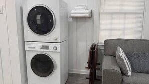 A laundry area with stacked washing machines and a grey couch with a pillow. - Rawson Circle Cottage (Albany)