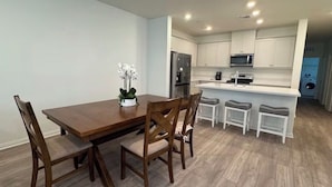 Una cocina moderna con armarios blancos, una mesa de comedor de madera y una pequeña isla con taburetes de bar.