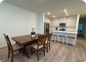 Una cocina moderna con armarios blancos, una mesa de comedor de madera y una pequeña isla con taburetes de bar.