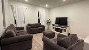 Una sala de estar moderna con un televisor de pantalla plana, dos sofás, una mesa de centro y una planta.