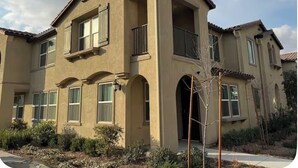 Una casa de dos pisos con fachada color beige, múltiples ventanas y un balcón.