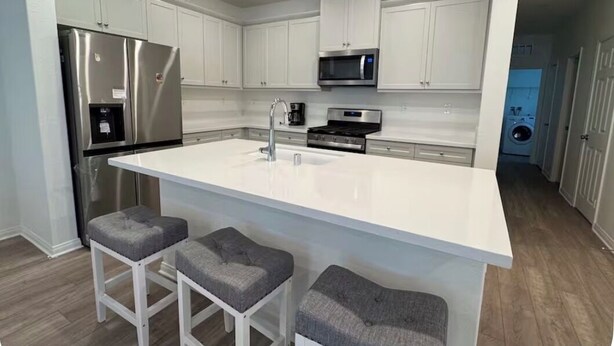 Una cocina moderna con armarios blancos, electrodomésticos de acero inoxidable y una isla central con taburetes de bar.