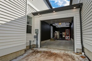 A garage entrance with a black interior wall, a ceiling light fixture, and a door leading to a driveway.