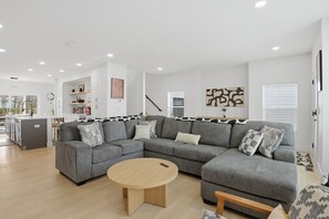A modern living room with a grey sectional sofa, a round wooden coffee table, and a kitchen in the background.