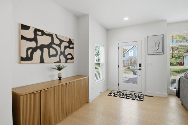 A modern interior with a wooden console, abstract art, a door with a glass panel, and a patterned rug.